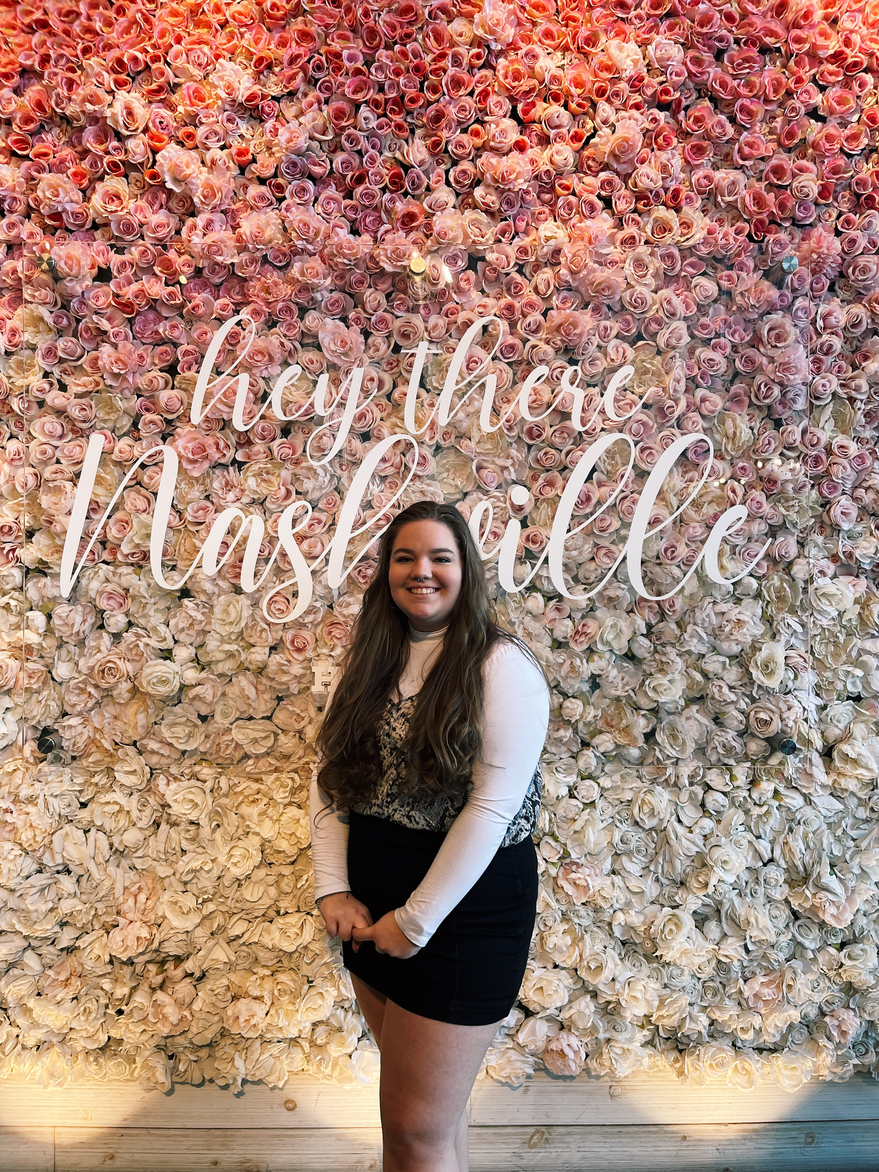 girl posing in front of white and pink rose wall with the words "hey there Nashville" in cursive