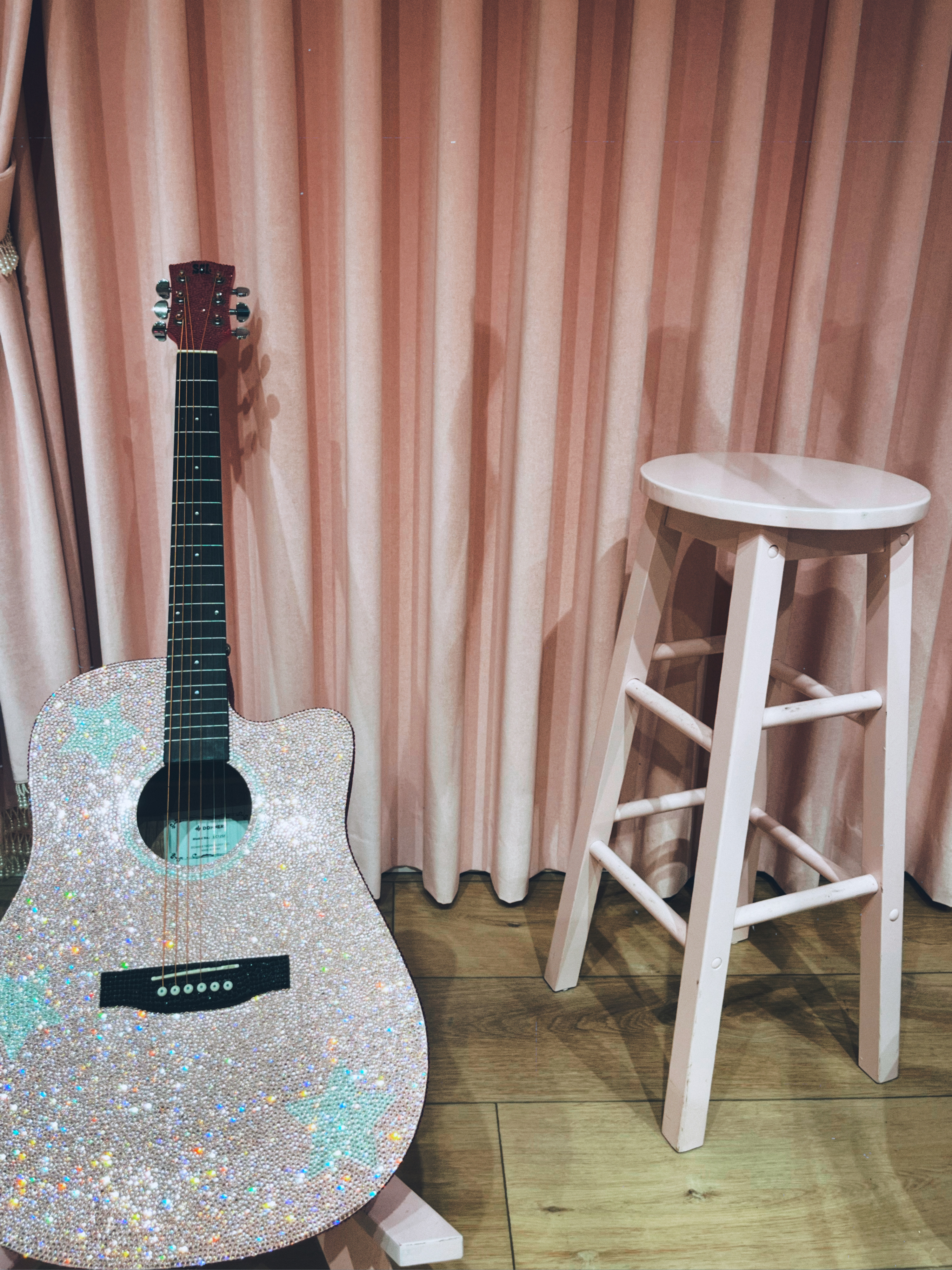 pink sparkly guitar next to a pink stool in front of pink curtains 