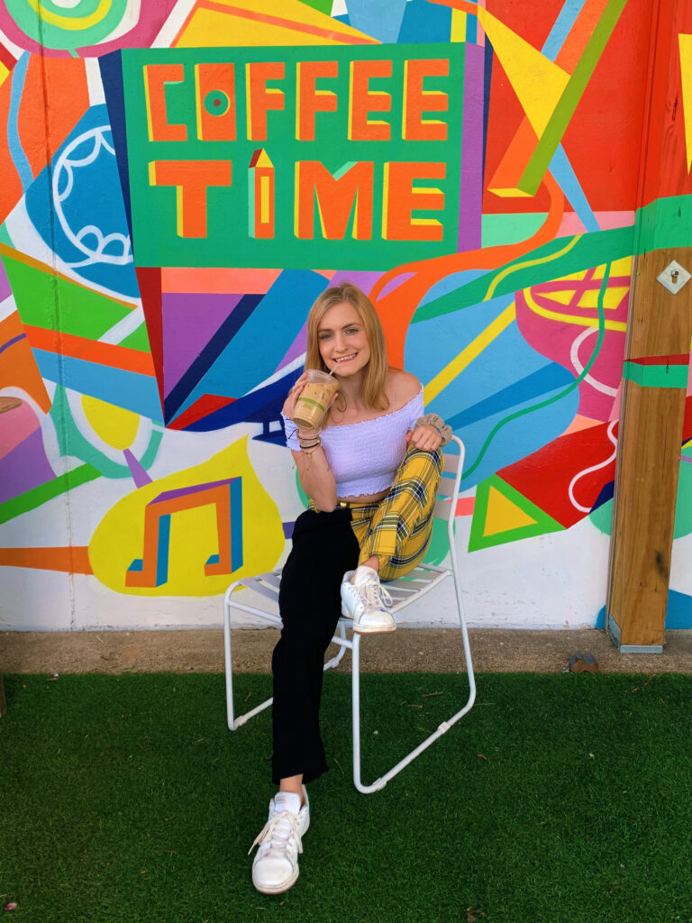 Girl sitting and drinking a coffee in front of Coffee Time Mural 
