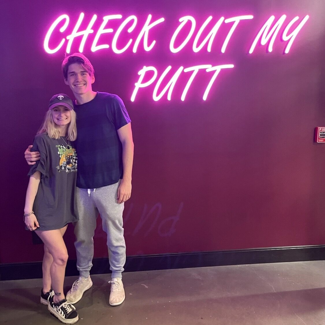 a couple standing infront of a neon sign that says Check Out My Putt at Puttshack in Atlanta 
