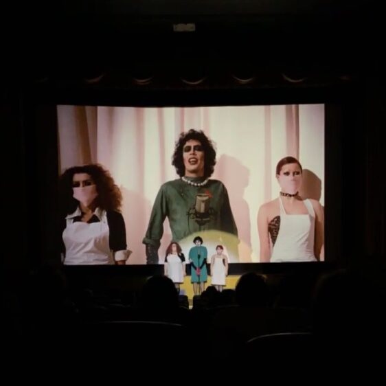 actors standing infront of a screen showing the Rocky Horror Picture Show 