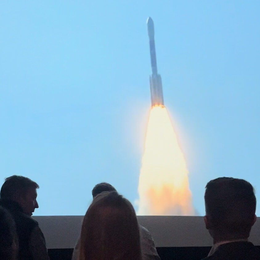 People watching a video of a rocket taking off at Fernbank After Dark 